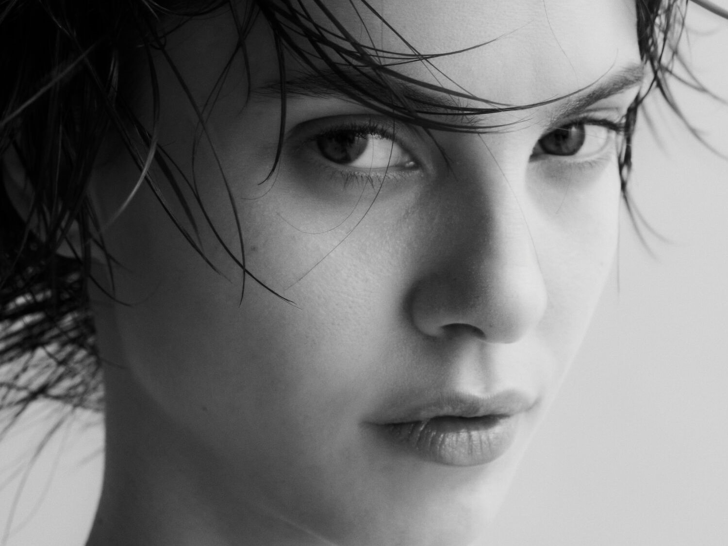 Nahaufnahme einer Frau mit nassen Haaren, die ihr Gesicht umrahmen, und einem intensiven Blick, der direkt in die Kamera gerichtet ist.