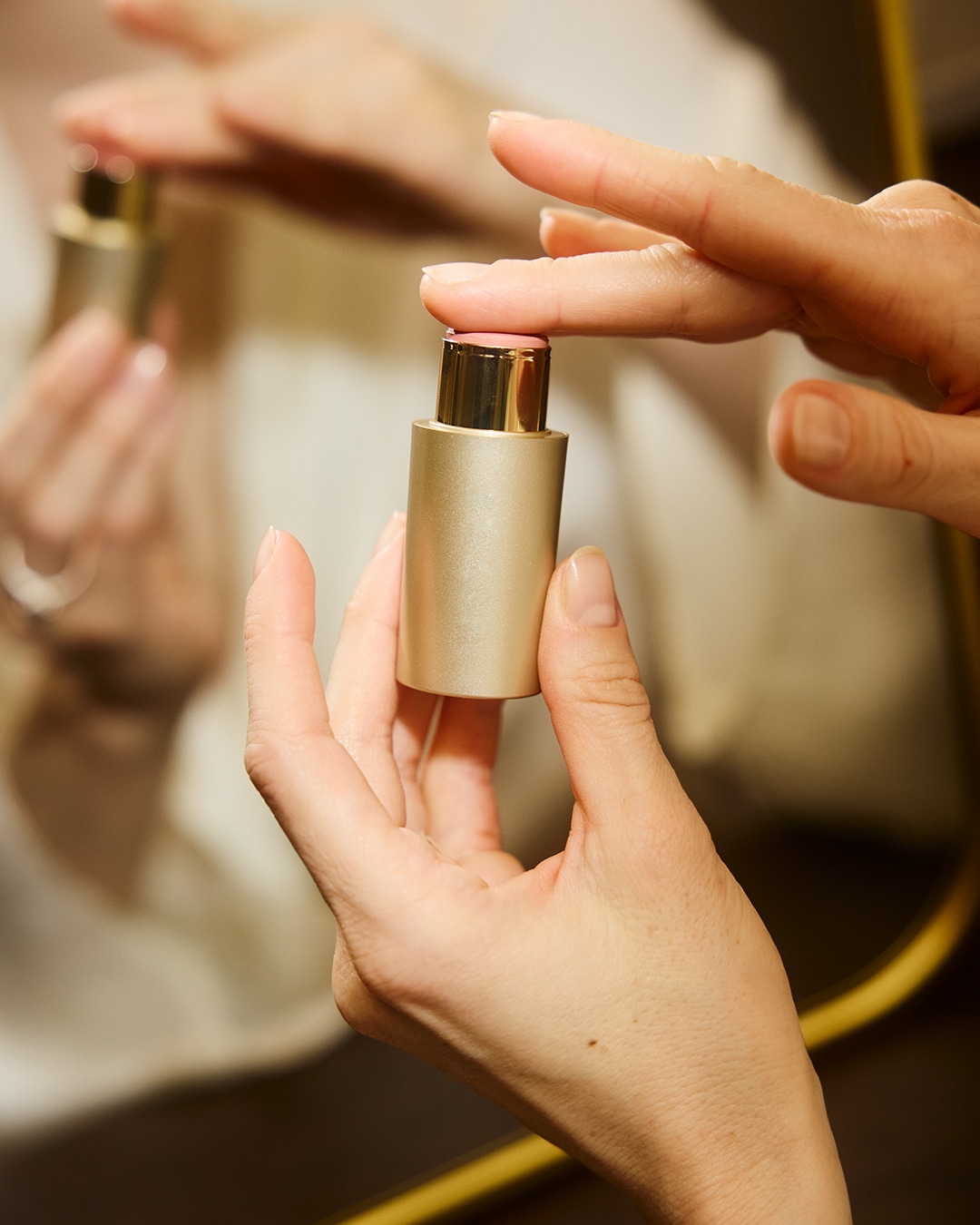 Een vrouw houdt een gouden make-upstick vast, klaar om de roze balsem aan te brengen voor een subtiele kleur.