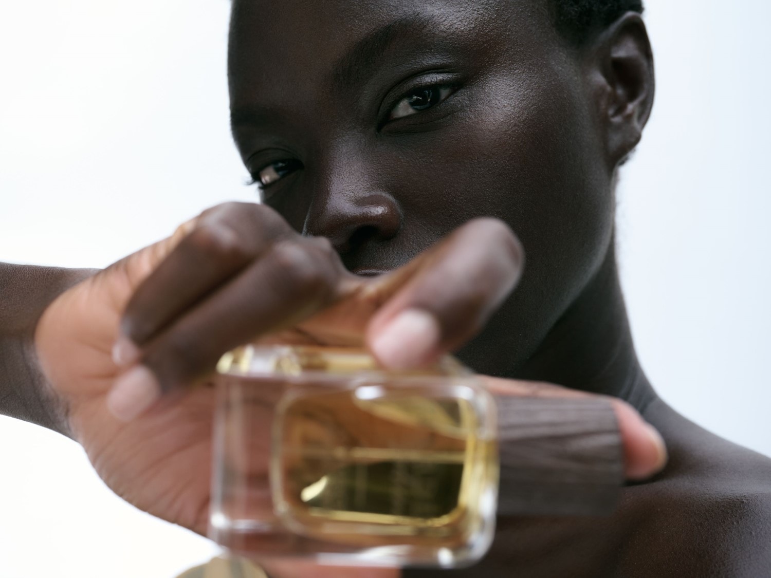 Eine Frau mit dunkler Haut hält einen transparenten Parfümflakon mit einem holzähnlichen Verschluss in der Hand.