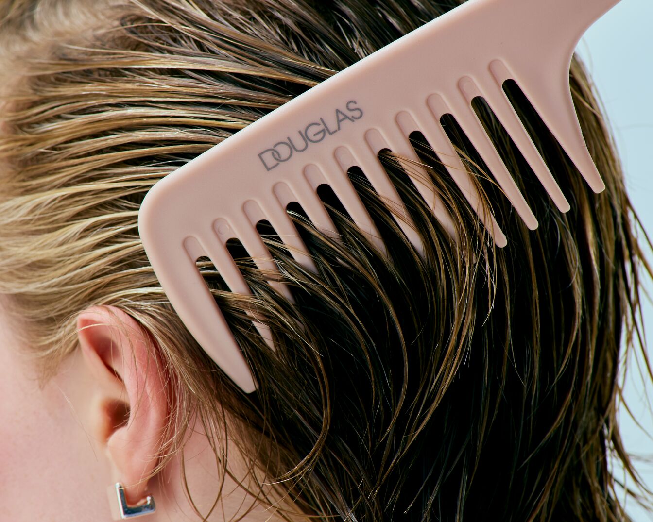 Nahaufnahme von nassem, braunem Haar, das mit einem hellrosa Douglas-Kamm gekämmt wird, der die Marke trägt.