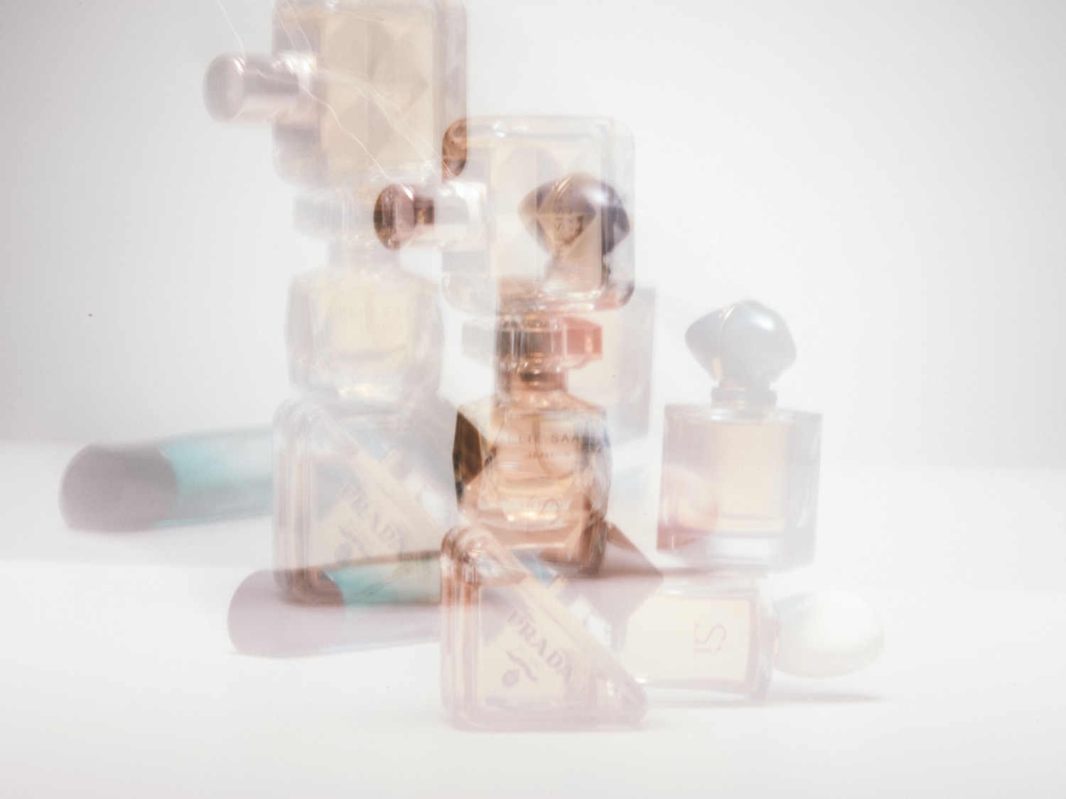 Verschillende parfumflesjes van merken als Prada, Elie Saab en Giorgio Armani staan op een witte achtergrond.