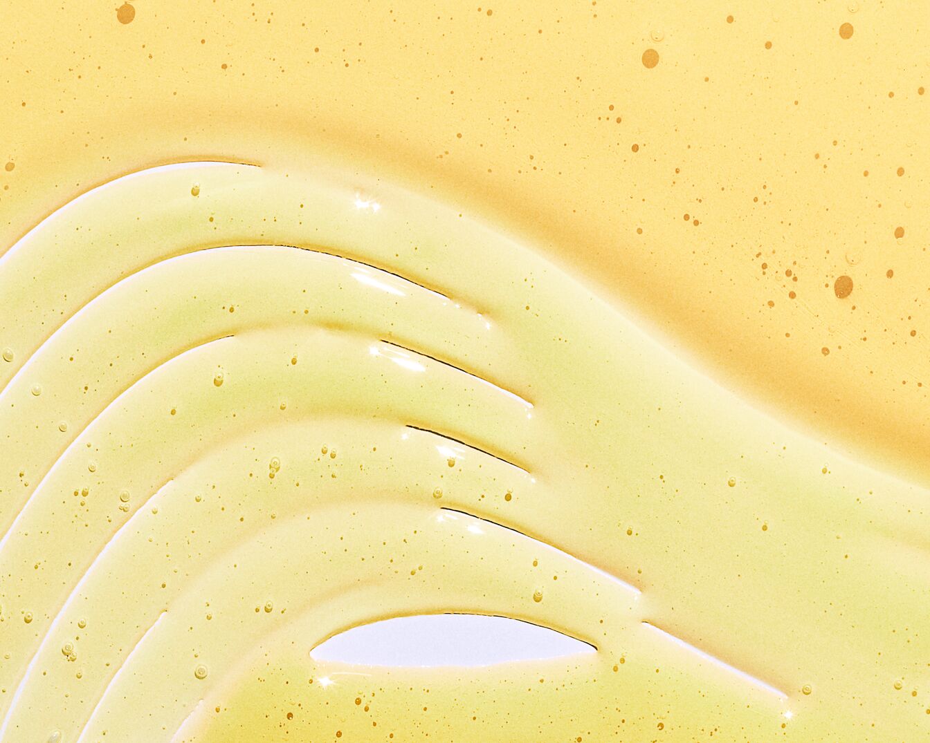 Texture dorata e lucida di un siero o olio cosmetico, steso in onde delicate su una superficie chiara, ideale per prodotti di bellezza e cura della pelle.