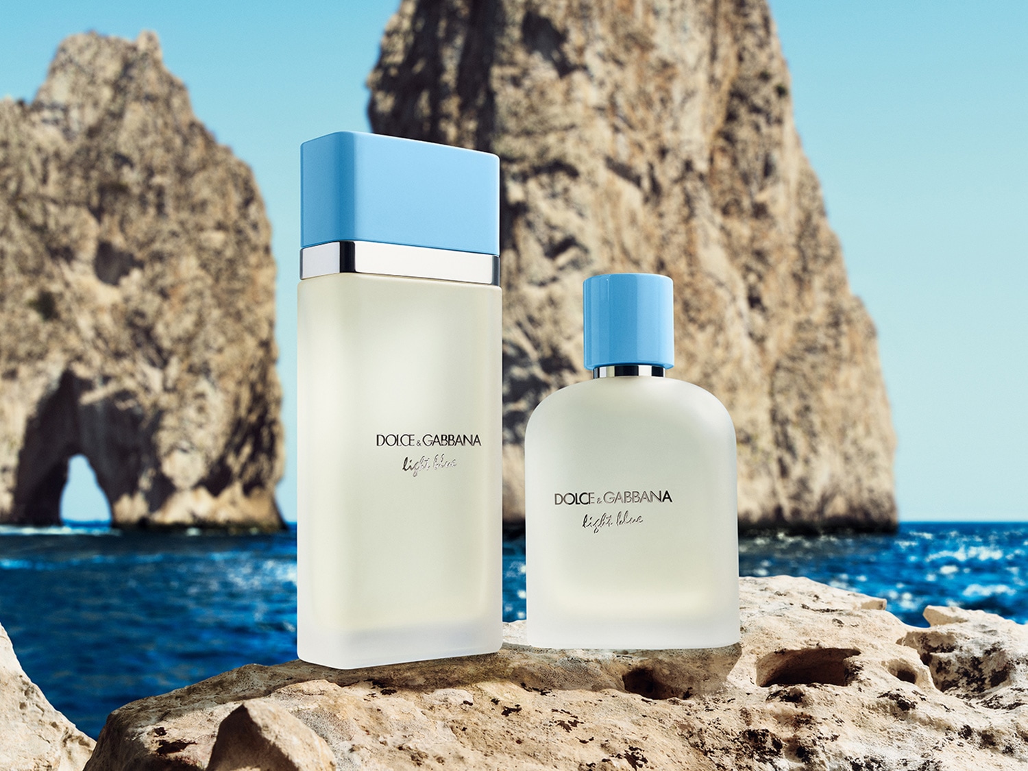 Zwei Dolce&Gabbana Light Blue Parfümflaschen stehen auf einem Felsen mit dem Meer und Felsformationen im Hintergrund.
