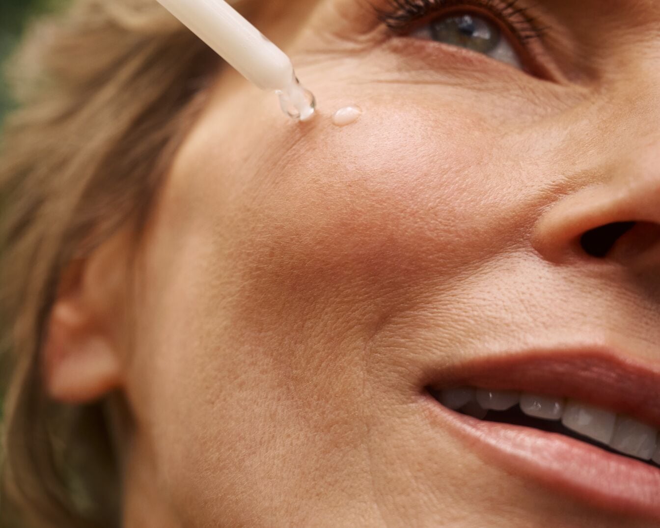 Nahaufnahme einer Frau, die sich mit einer Pipette ein Serum auf die Wange aufträgt, um die Haut zu pflegen.