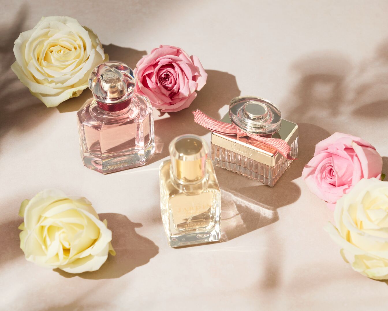 Découvrez un assortiment exquis de parfums, chacun dans un flacon unique, entouré de roses délicates aux teintes douces, créant une ambiance olfactive et visuelle captivante.