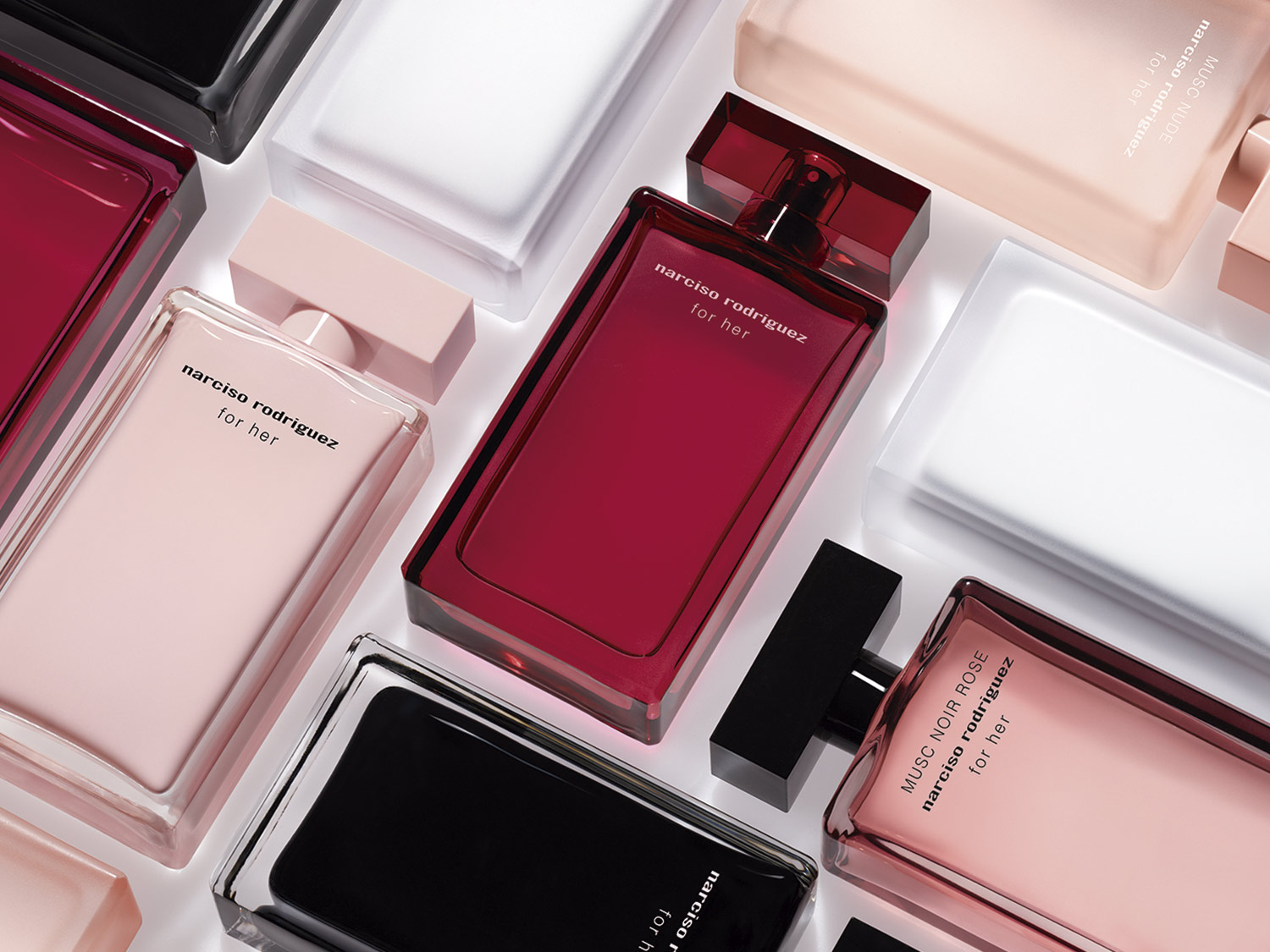 Una colección de frascos de perfume Narciso Rodriguez 'for her' en varios tonos como rosa, rojo y negro, sobre un fondo blanco.