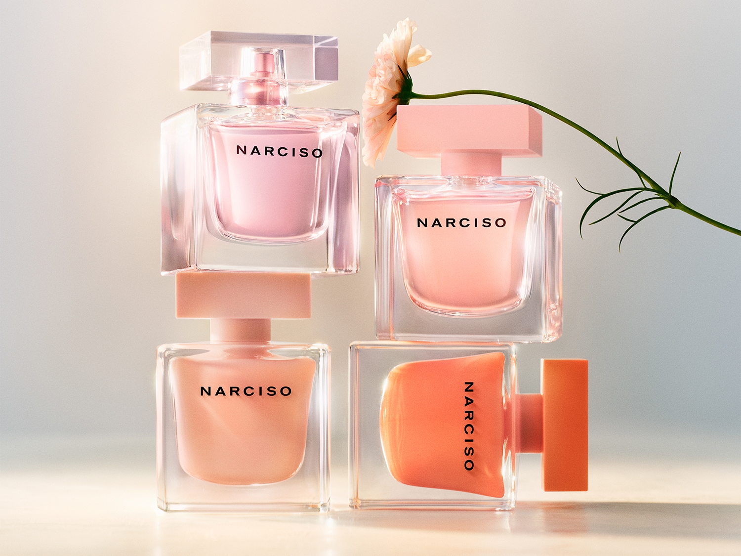 Cuatro frascos de perfume Narciso se apilan uno encima del otro, mostrando tonos rosas y melocotón, con una flor delicada que añade un toque de elegancia.