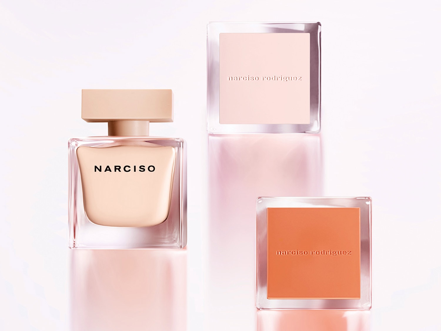 El perfume Narciso Rodriguez en un frasco transparente con un tapón color crema, junto a dos frascos cuadrados con tonos melocotón y rosa pálido.