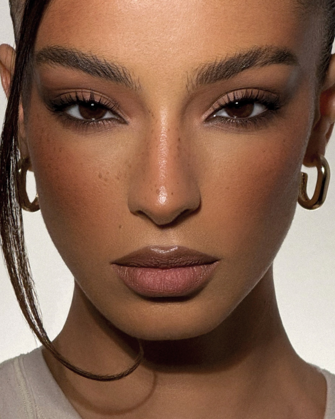 Primer plano del rostro de una mujer con maquillaje neutro, resaltando sus ojos marrones con sombras oscuras y labios brillantes.