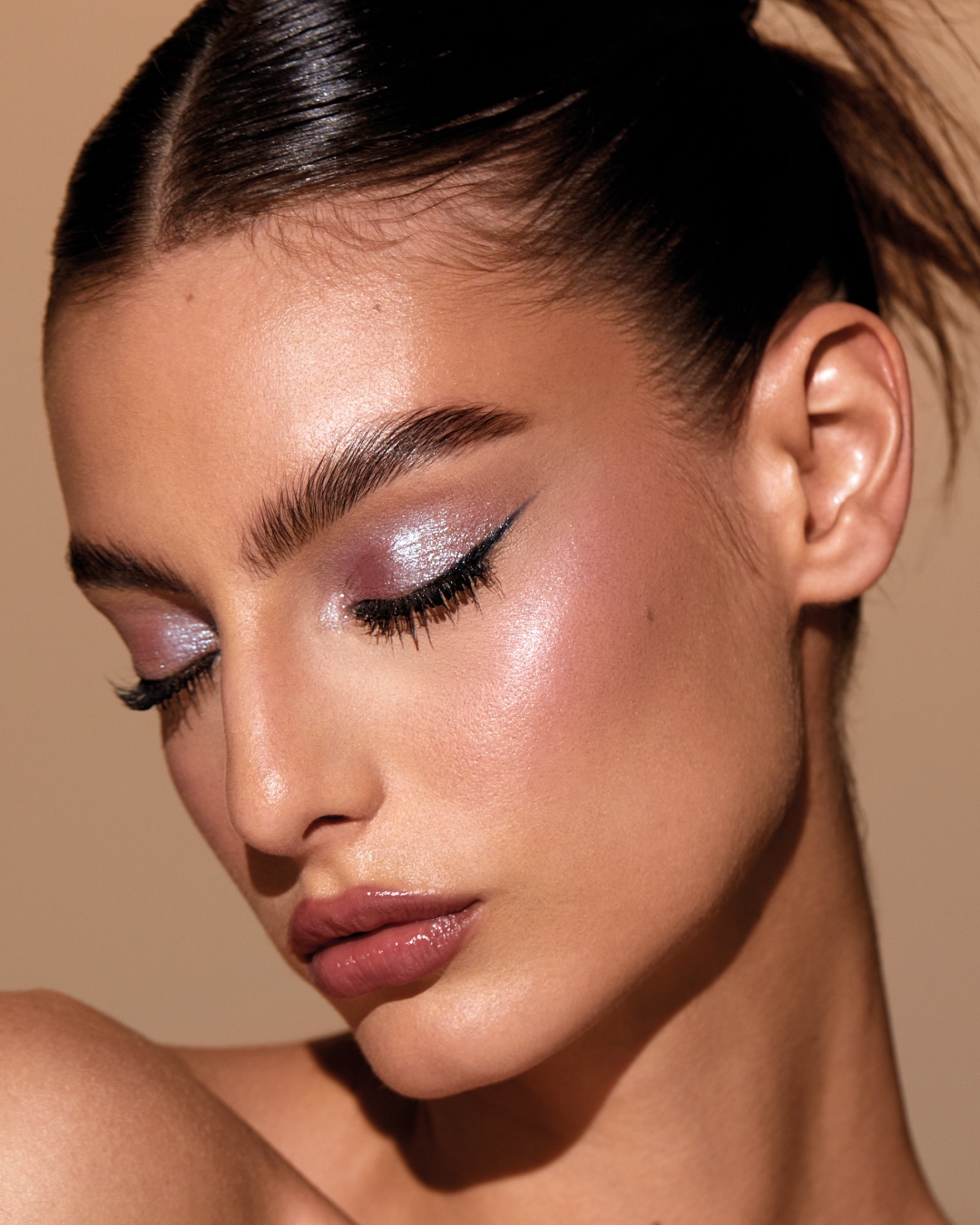 Primer plano de una mujer con sombra de ojos brillante color lavanda, delineador de ojos negro y labios color malva brillante.