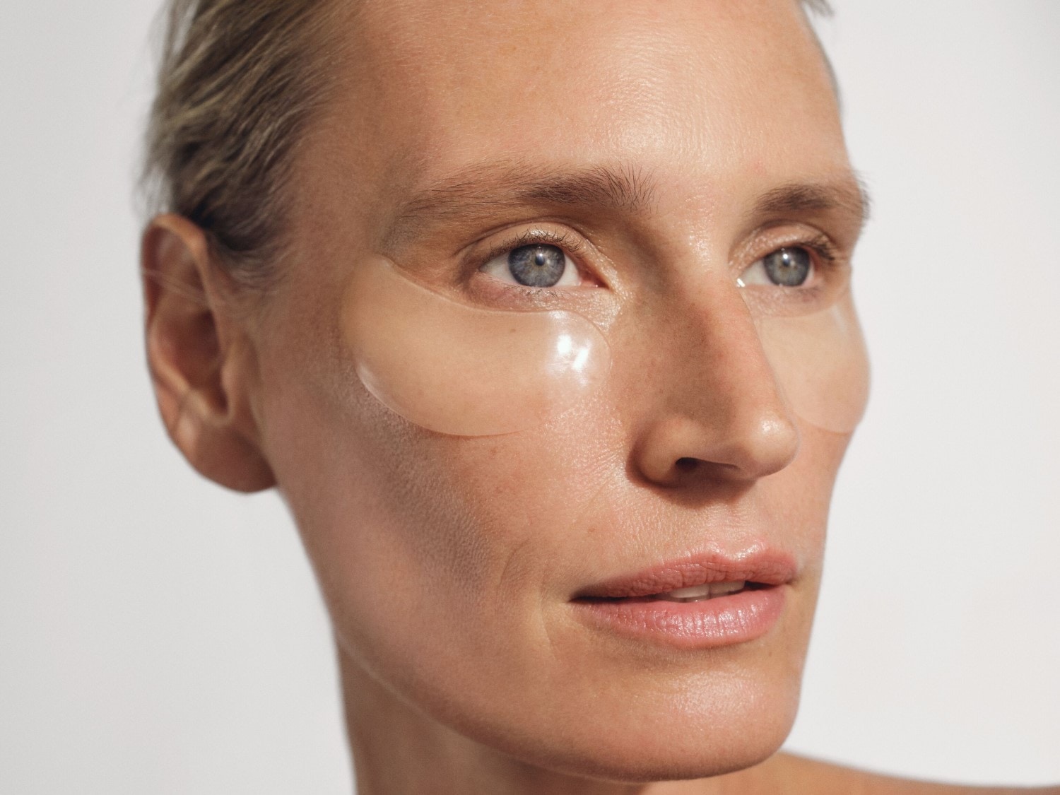 Moters veidas su šviesiais plaukais ir paakių pagalvėlėmis, skirtomis odos priežiūrai.