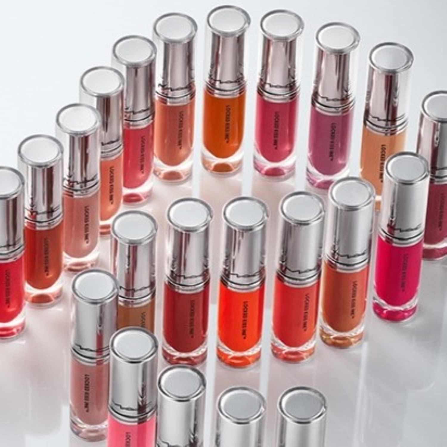 Eine Sammlung von MAC Locked Kiss Ink Lippenstiften in verschiedenen Farbnuancen, von sanften Rosatönen bis hin zu kräftigem Rot, präsentiert in silberfarbenen Verpackungen.