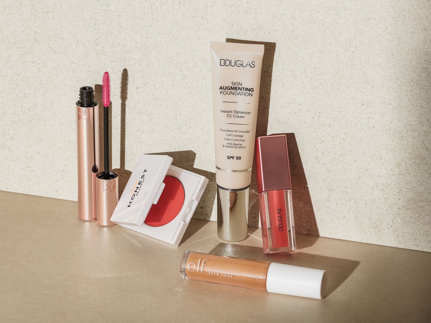 Kosmetikos rinkinys, įskaitant „Douglas“ odos stiprinamąjį pagrindą, „Honest Beauty“ skaistalus, „elf“ maskuoklį ir „Douglas“ lūpų blizgį.