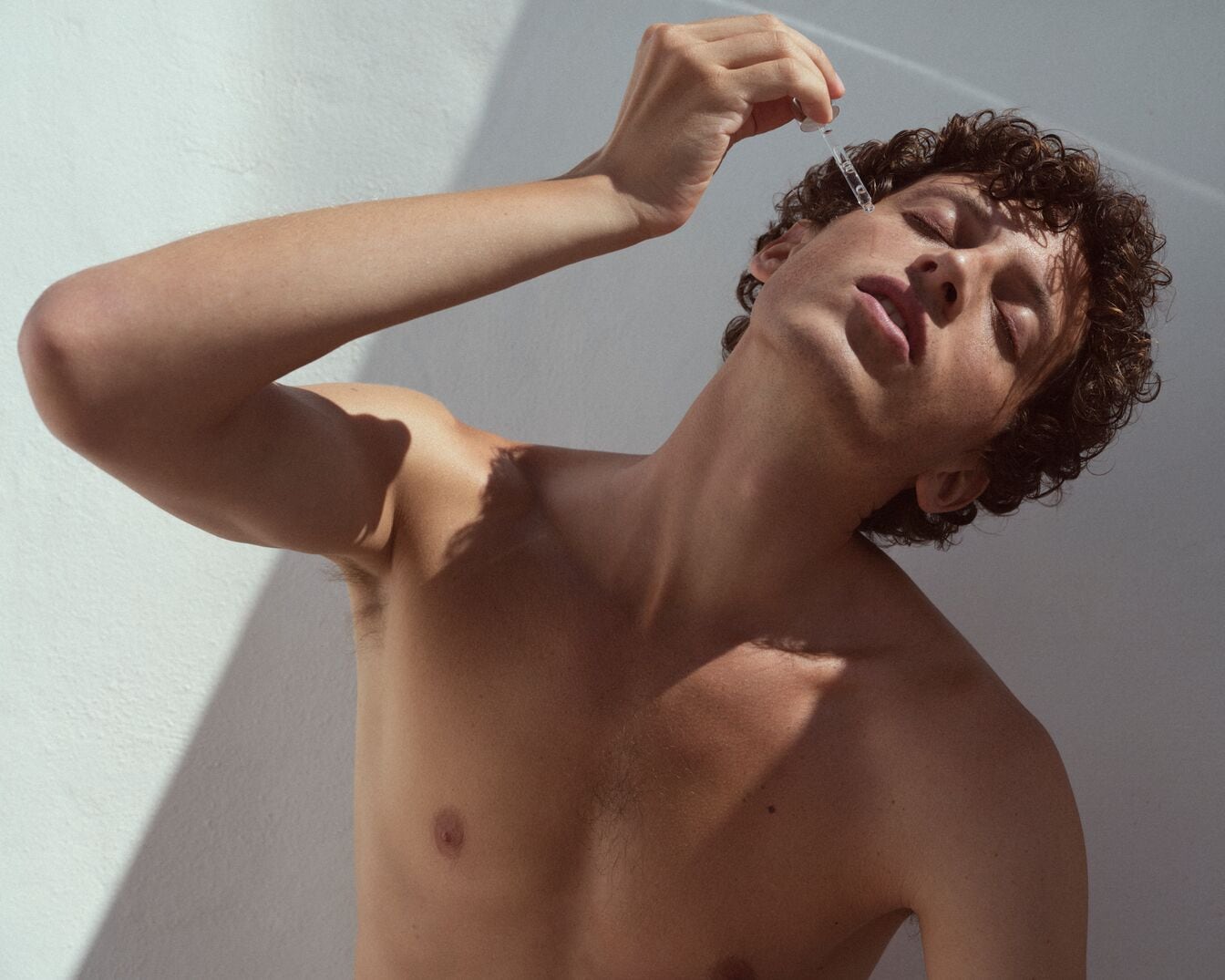 Vyras be marškinių tepa skystį ant veido pipete, kad oda būtų sveika ir spindinti.