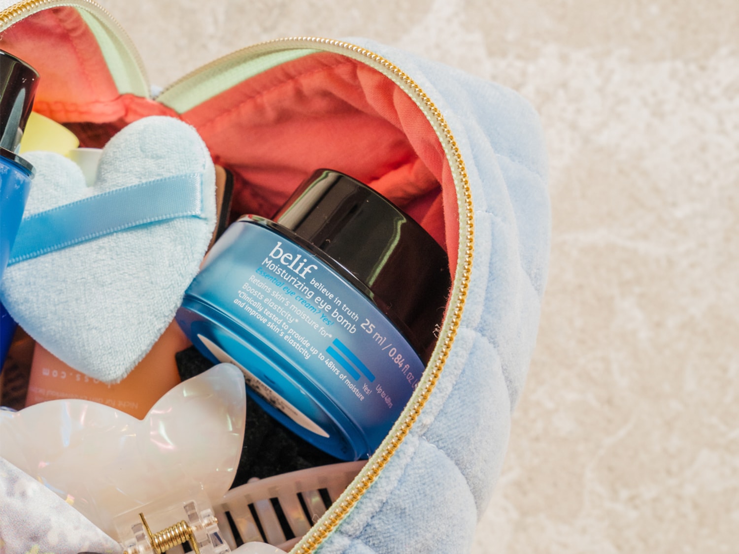 In een lichtblauwe make-uptas zit een potje Belif Moisturizing Eye Bomb, die de huid tot 48 uur hydrateert en de elasticiteit verbetert.