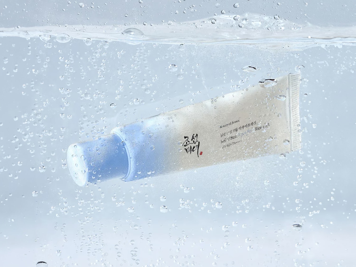 Tube blanc de crème solaire Beauty of Joseon Rice SPF50+ PA++++ flottant dans l'eau avec des bulles, promettant une protection solaire et une hydratation légères.