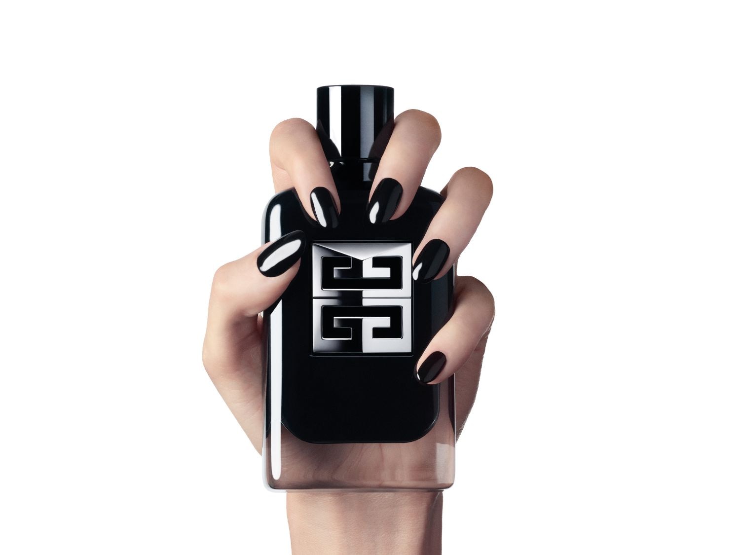 Main tenant un flacon de parfum noir élégant avec le logo argenté de Givenchy, les ongles vernis en noir brillant.