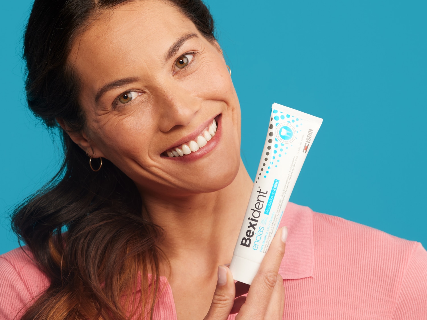 Una mujer sonriente sostiene la pasta de dientes Bexident Encías de ISDIN, que promete resultados en 2 días con su triple acción antiplaca y antioxidante.