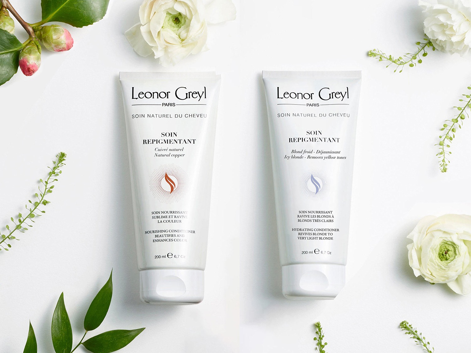 Dwa białe opakowania Leonor Greyl Soin Repigmentant: jeden w odcieniu miedzi, drugi w chłodnym blondzie, otoczone kwiatami i zielonymi gałązkami.