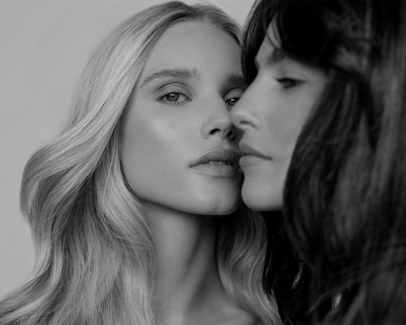 Portret dwóch kobiet o różnych odcieniach włosów, z których jedna ma jasne, falujące włosy, a druga ciemne, proste włosy, obie z delikatnym makijażem.