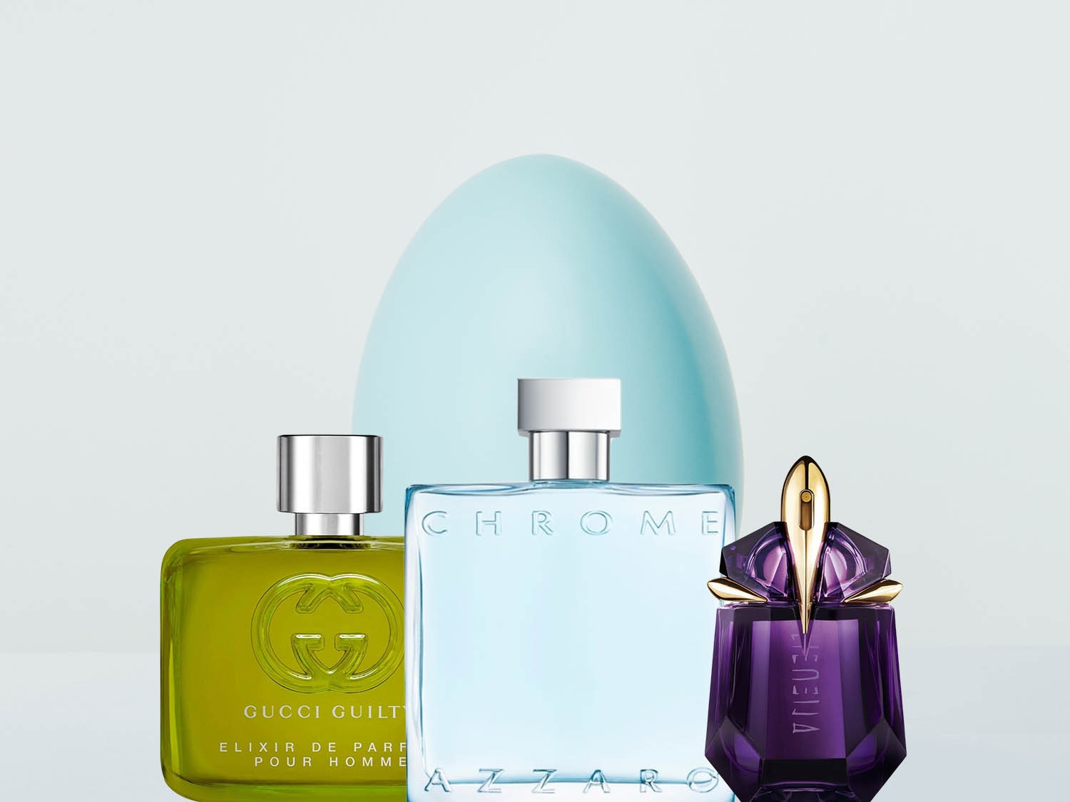 Trzy flakony perfum: Gucci Guilty w zielonym flakonie, Azzaro Chrome w błękitnym i Alien w fioletowym, na tle błękitnego kształtu przypominającego jajo.