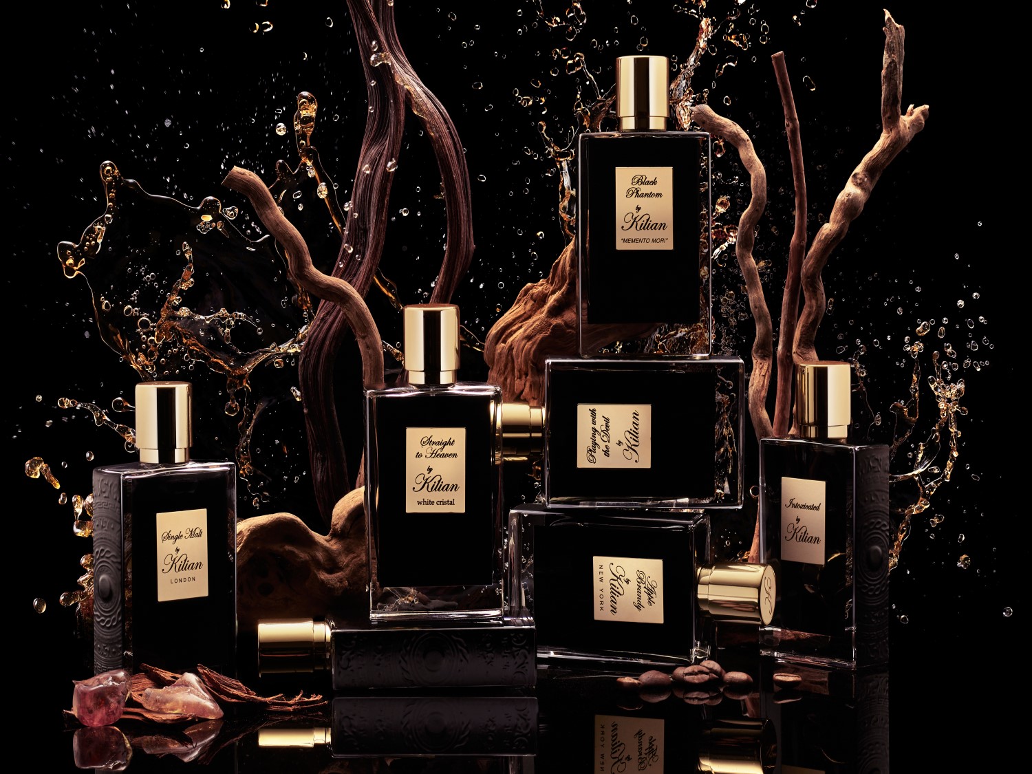Na czarnym tle, woda rozpryskuje się wokół kolekcji flakonów Kilian o różnych zapachach, takich jak Single Malt London i Straight to Heaven, z drewnianymi elementami dekoracyjnymi.