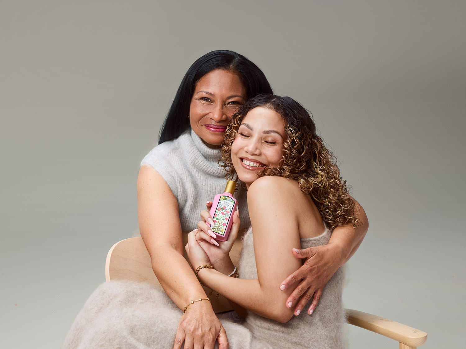 Une mère et sa fille sourient en se tenant enlacées, la fille tenant un flacon rose de Gucci Flora avec des motifs floraux.