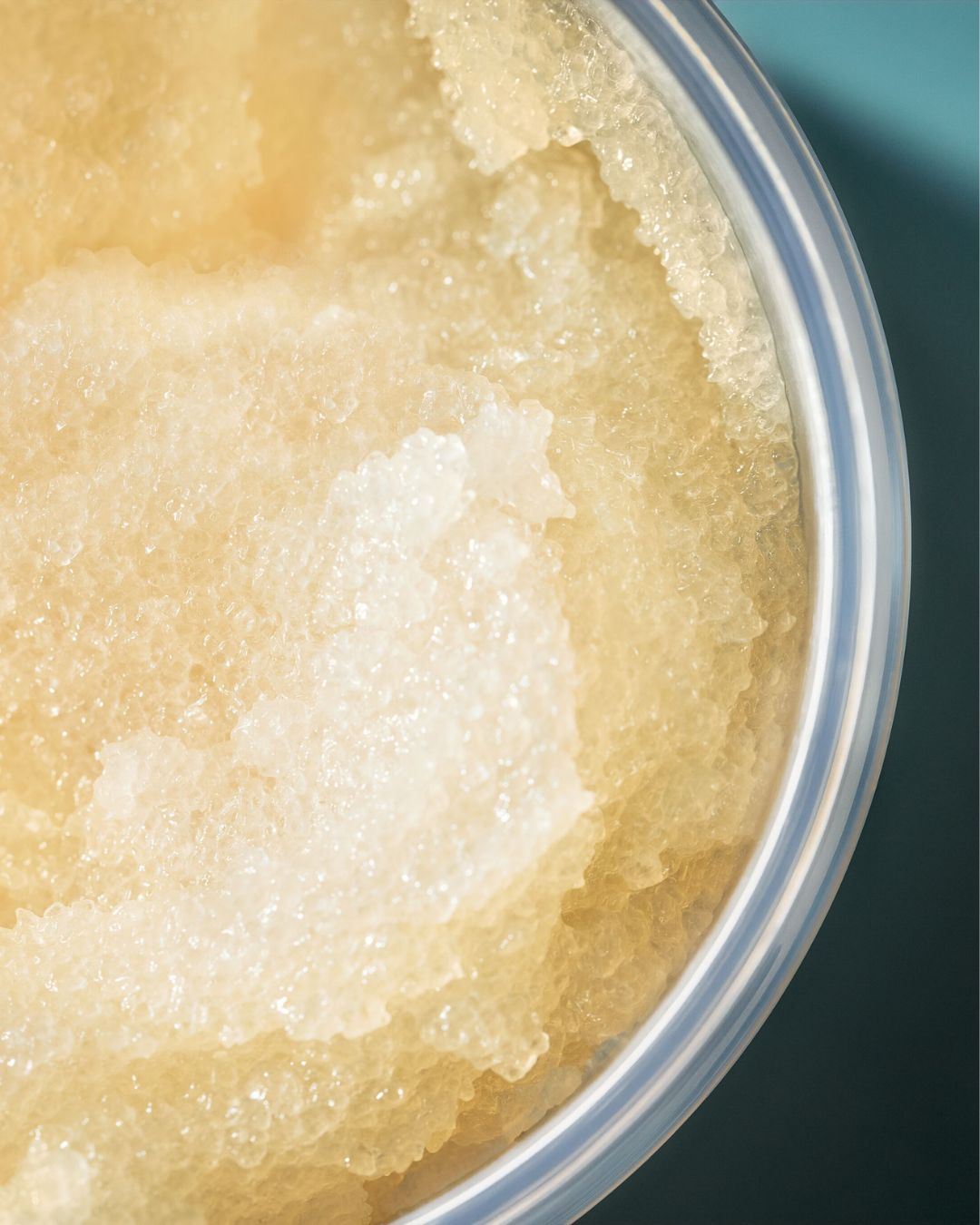 Detailní pohled na žlutý cukrový peeling v průhledné nádobě, který slibuje hladkou a zářivou pokožku.