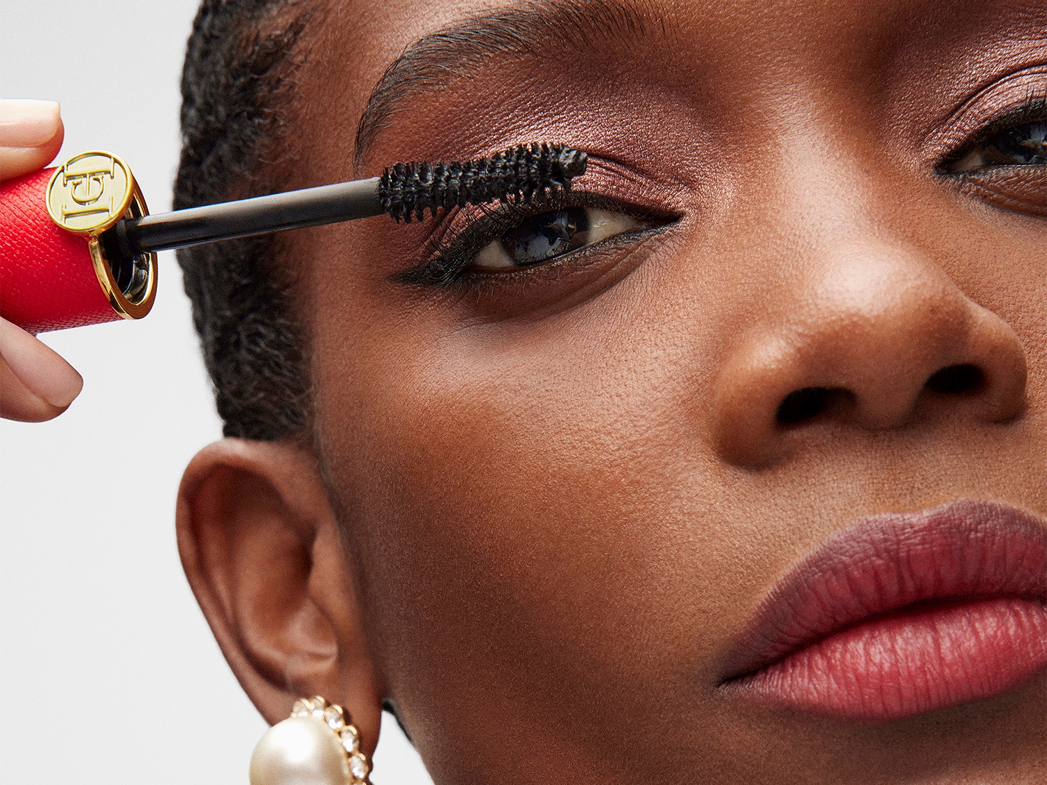 Nahaufnahme einer Frau, die sich mit einer roten Mascara mit goldenem Detail die Wimpern tuscht, um einen glamourösen Augenaufschlag zu erzielen.