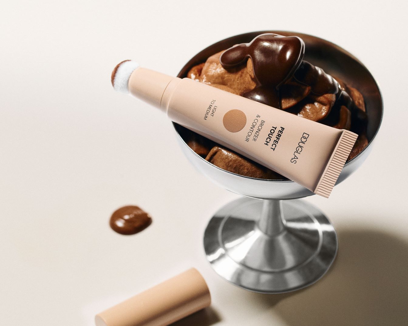 Douglas Perfect Touch Bronzer & Contour in hell- bis mittelbraun, liegt auf einem silbernen Eisbecher mit Schokoladenmousse und Soße.