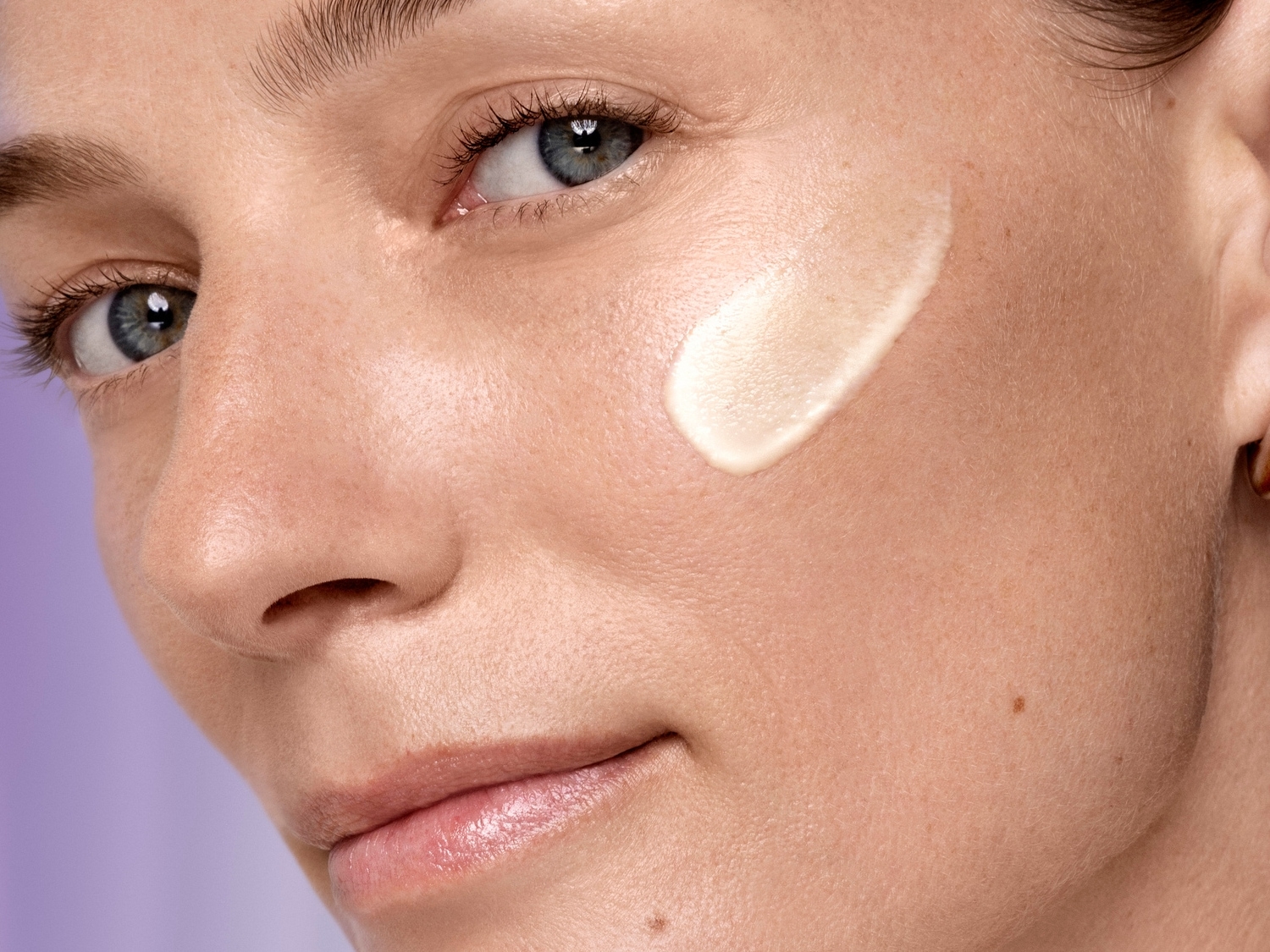 Detailný záber na tvár ženy s kvapkou svetlého krému na líci, ktorý zvýrazňuje jej prirodzenú krásu a zdravú pleť.