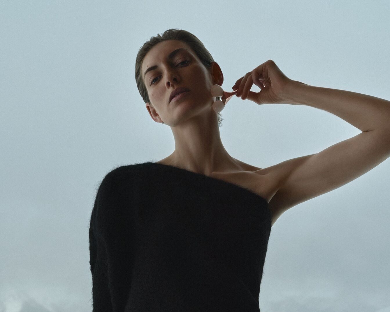 Eine Frau mit einem schwarzen, schulterfreien Oberteil benutzt einen Gesichtsroller, um ihre Haut zu pflegen.