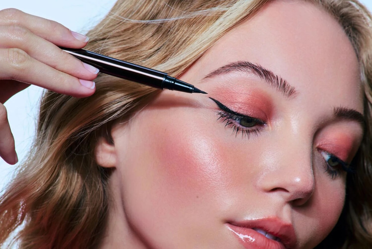 Een vrouw met blond haar brengt zwarte eyeliner aan met een zwarte eyelinerpen voor een strakke, gevleugelde look.