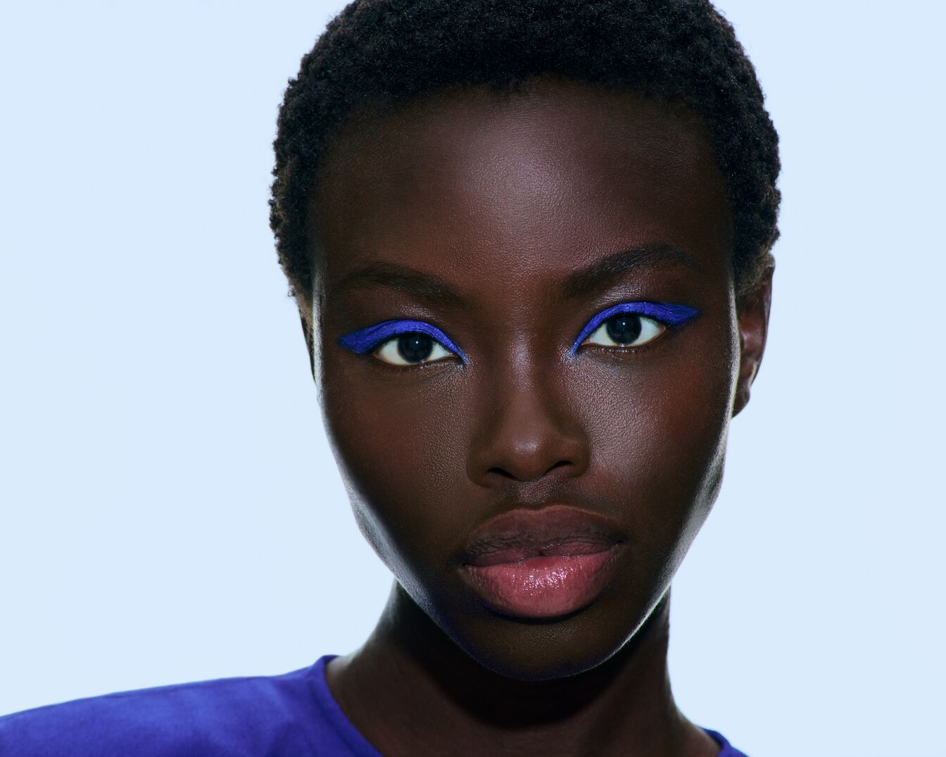 Een close-up van een vrouw met een donkere huid en blauwe eyeliner, die een gedurfde en opvallende make-up look creëert.