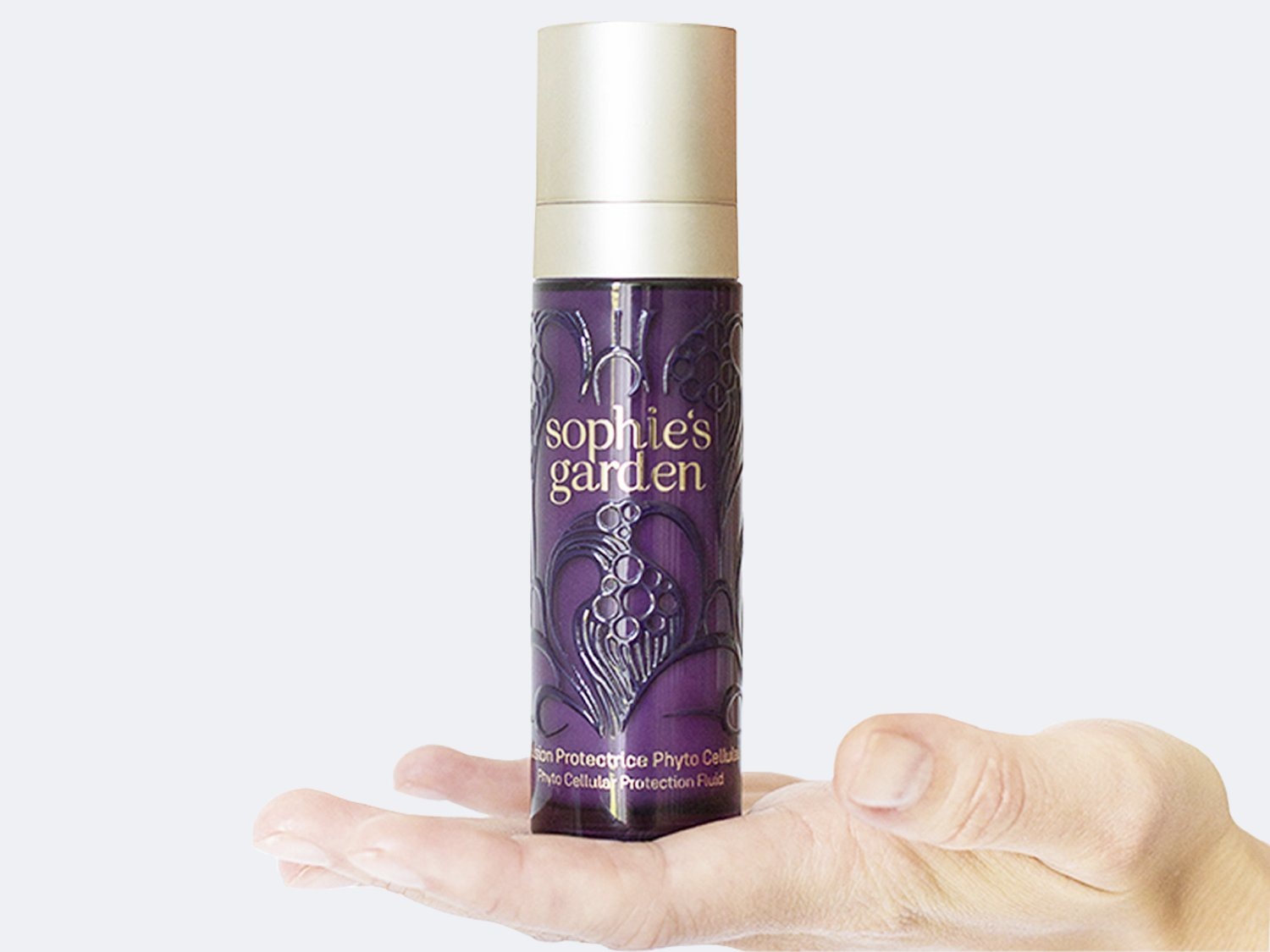 Aquí se muestra un frasco de fluido de protección celular fito de Sophie's Garden, con un elegante diseño floral plateado sobre un fondo morado intenso y un tapón dorado.