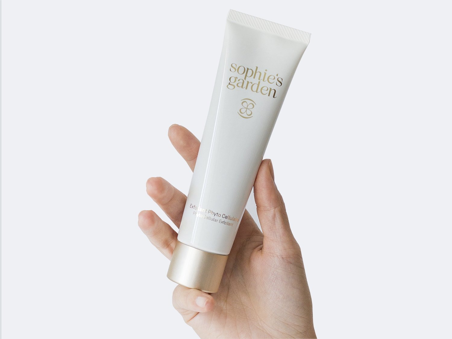 Aquí se muestra un tubo blanco de Sophie's Garden Exfoliant Phyto Cellular, sostenido por una mano, con letras doradas.