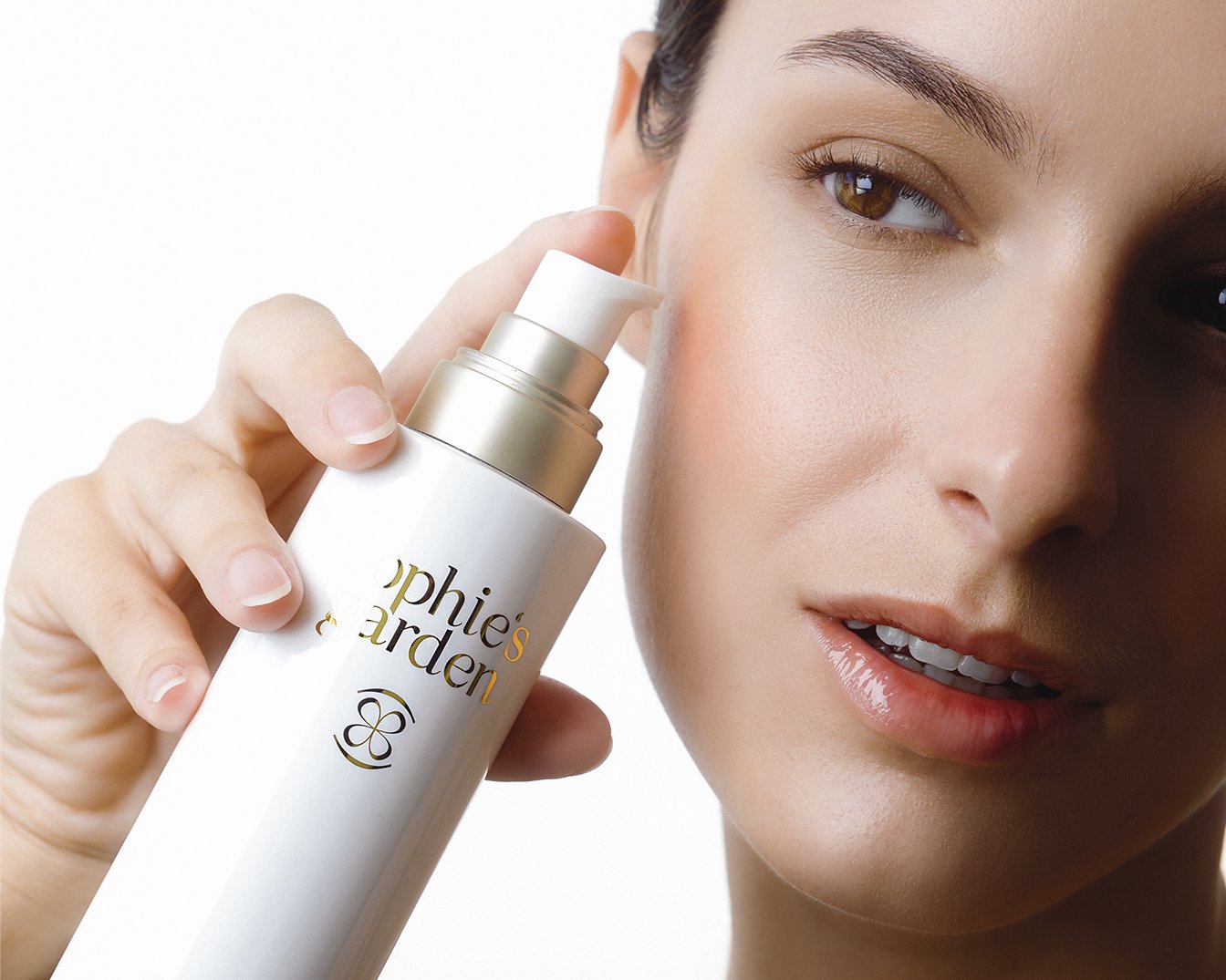 Una mujer sostiene una botella blanca de Sophie's Garden con letras doradas, lista para aplicar el producto en su rostro, mostrando una piel radiante y saludable.