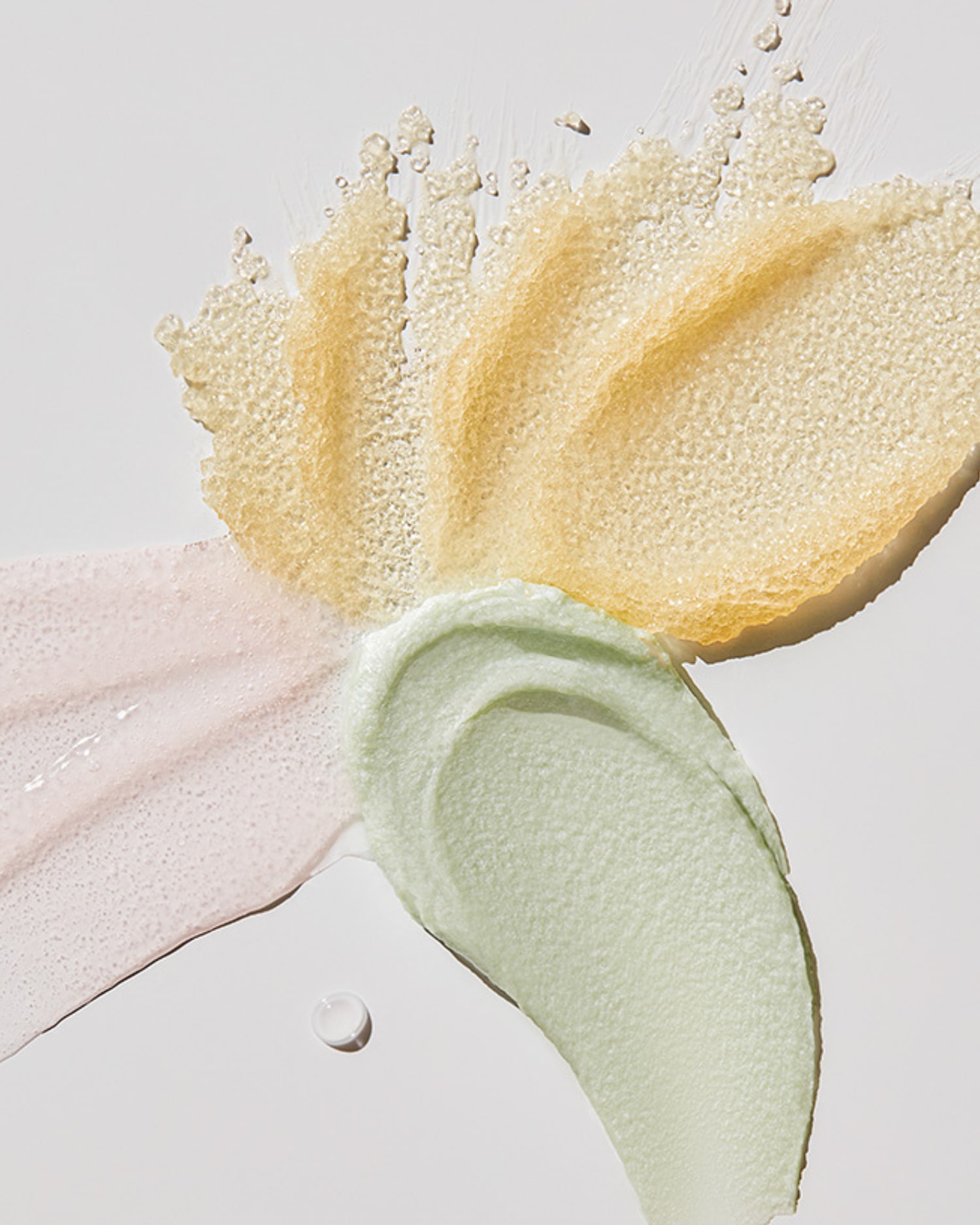 Nahaufnahme von Texturen in Gelb, Grün und Rosa, die verschiedene Kosmetikprodukte darstellen.