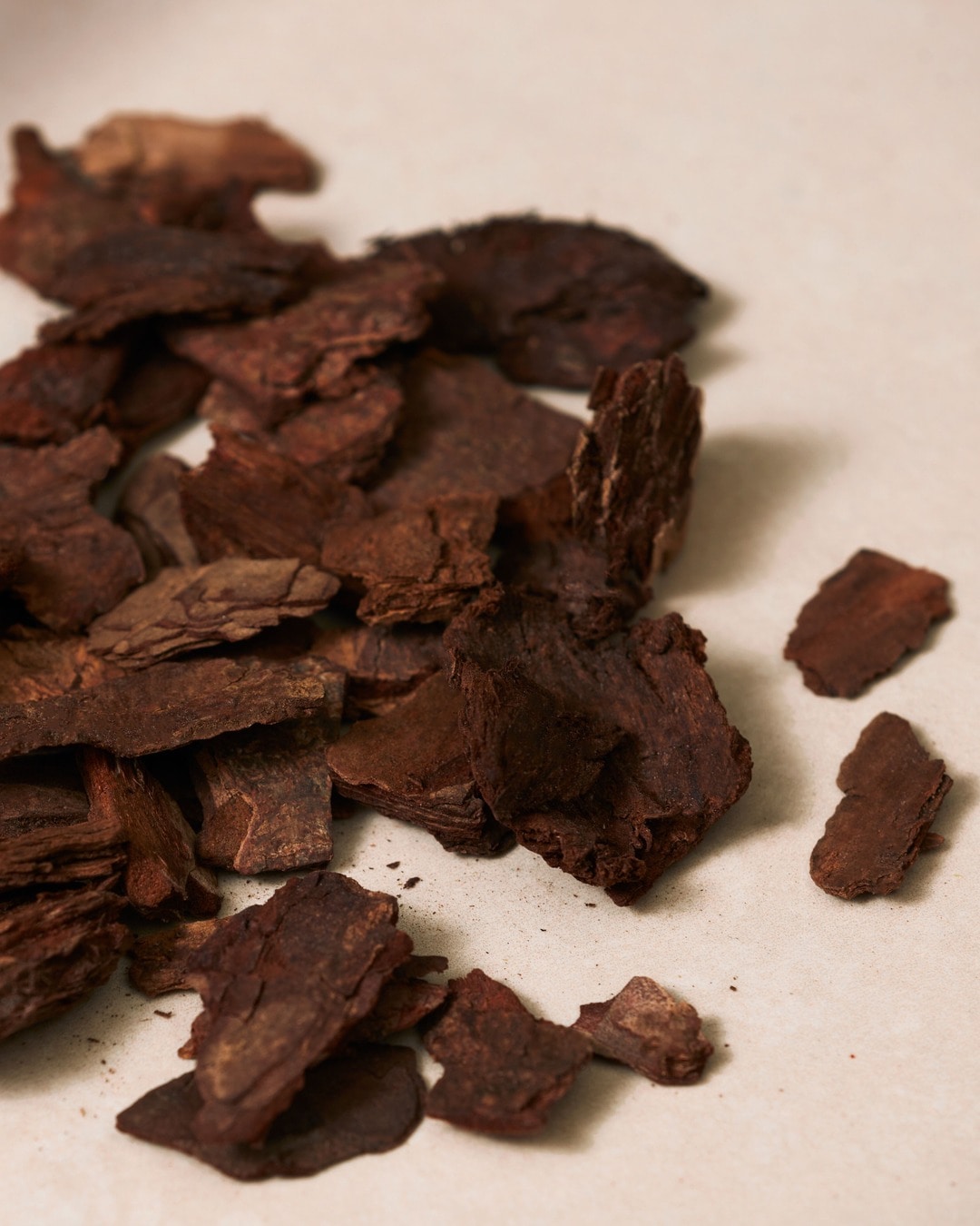 Štai tamsiai rudos spalvos medžio žievės gabalėlių krūva, išsidėsčiusi ant šviesaus paviršiaus.