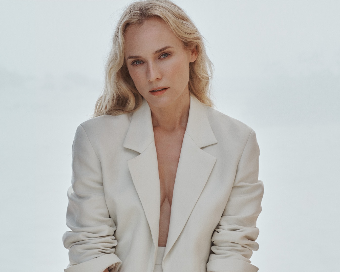 Een blonde vrouw met blauwe ogen draagt een crèmekleurig jasje en kijkt recht in de camera.