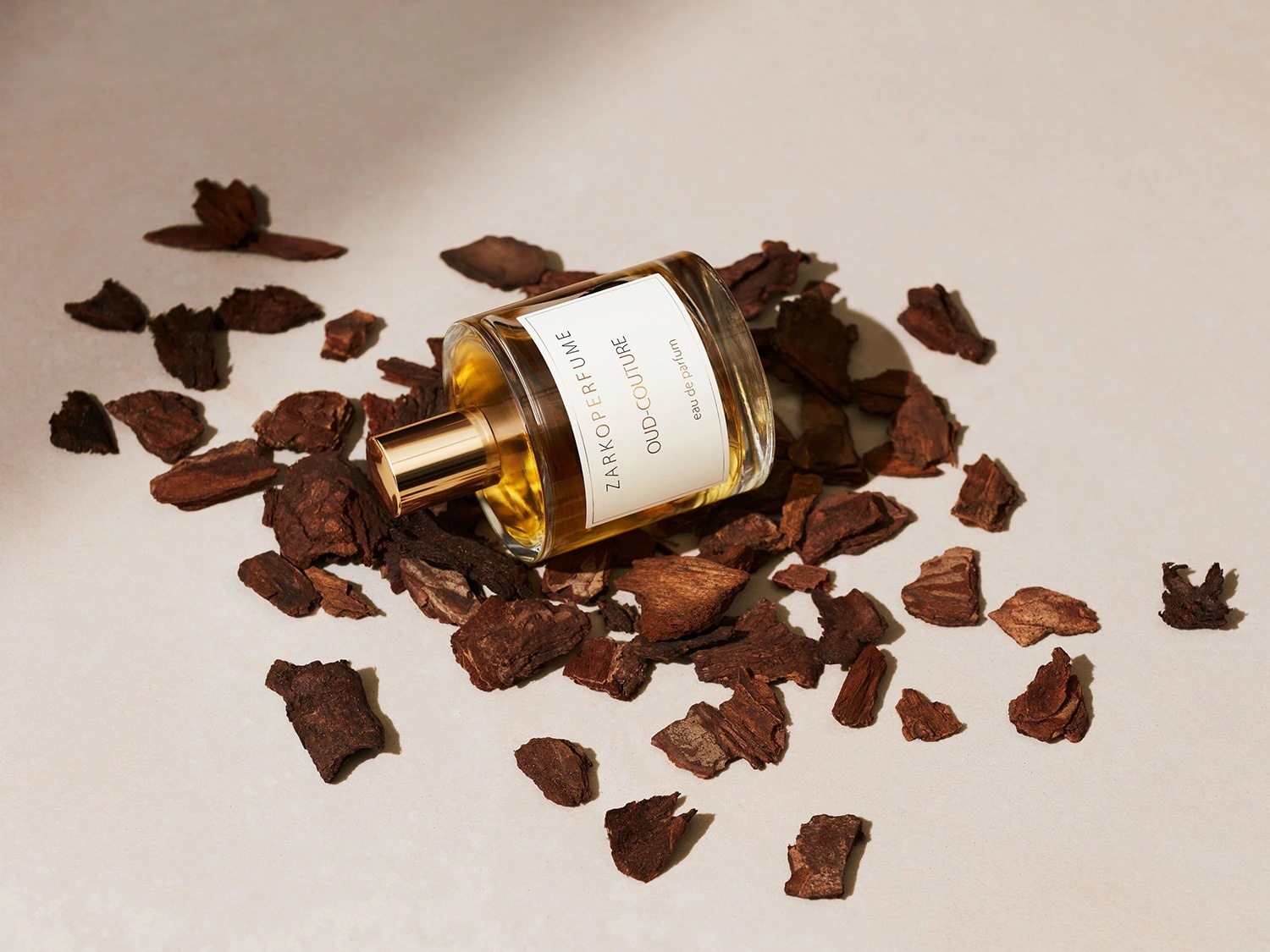 Flacone di profumo Zarkoperfume Oud-Couture Eau de Parfum, adagiato su frammenti di legno scuro, con tappo dorato e liquido ambrato visibile.