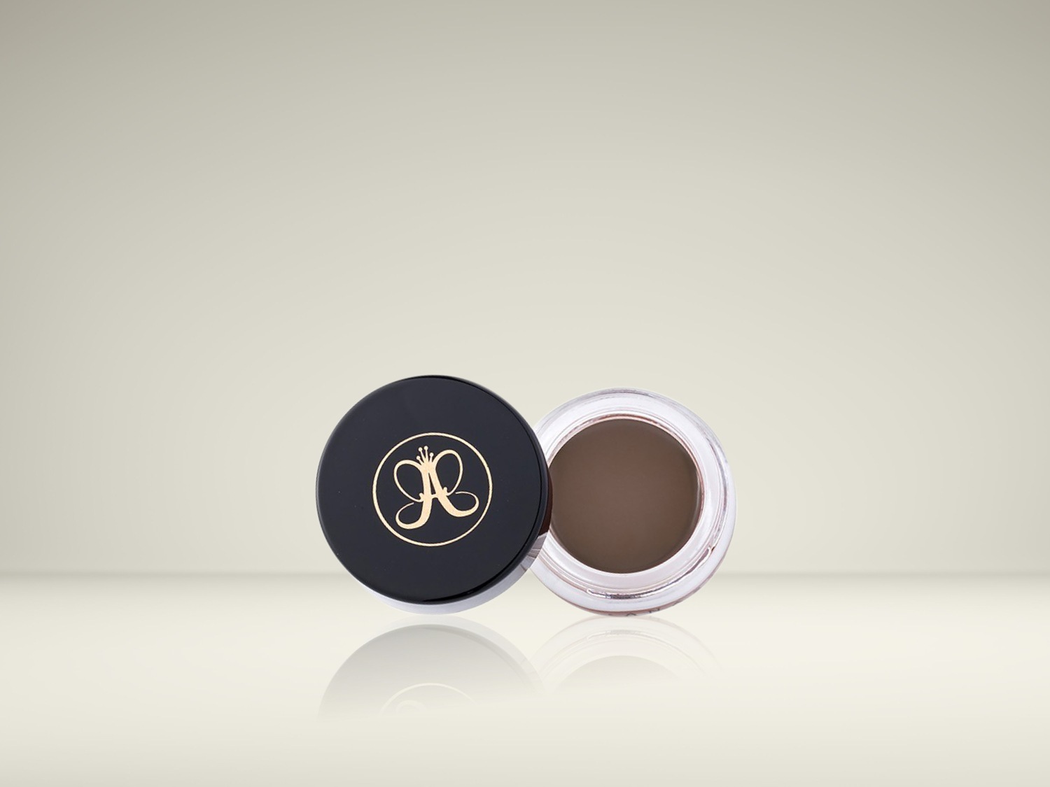 De Anastasia Beverly Hills Dipbrow Pomade in een open, transparant potje met een zwarte deksel ernaast, toont de rijke bruine kleur van de wenkbrauwpommade.