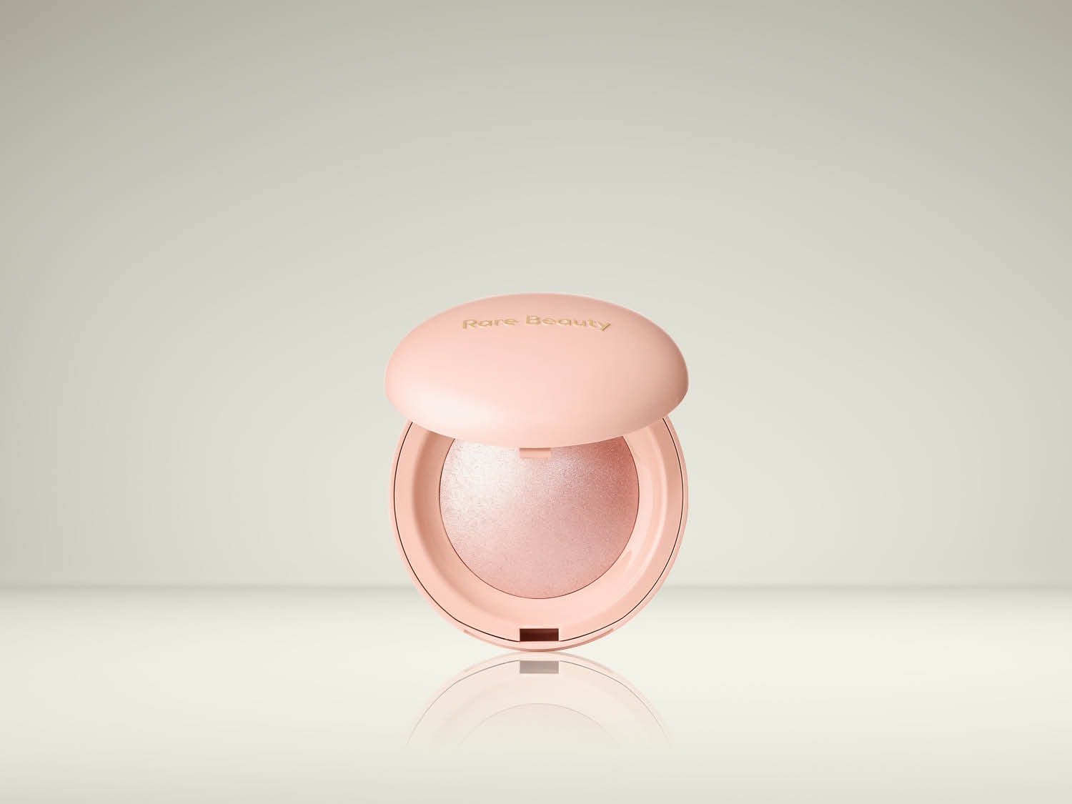 De Rare Beauty Soft Pinch Luminous Powder Blush in een open, lichtroze compact met een glinsterende blush, perfect voor een stralende gloed.