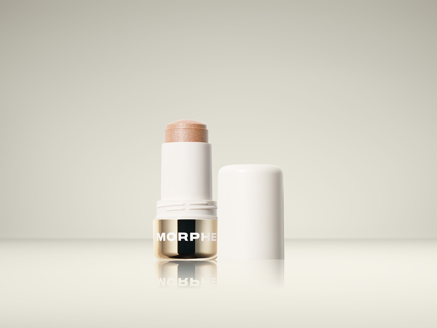 De Morphe Glow Show Radiant Highlighter Stick in een witte verpakking met gouden accenten, toont een glinsterende, lichtbruine tint die klaar is om de huid te laten stralen.