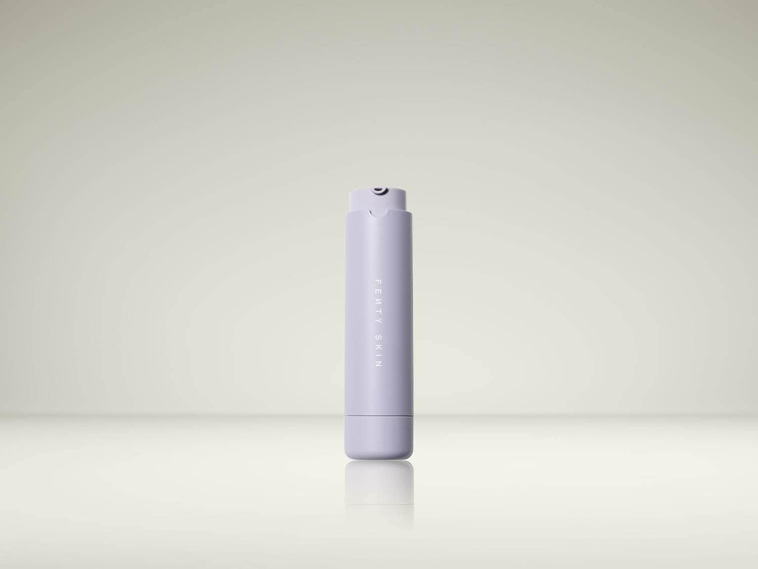 De Fenty Skin Fat Water Hydrating Milky Toner Essence is een langwerpige, lichtpaarse fles met de merknaam verticaal in het midden, staand op een glanzend oppervlak.
