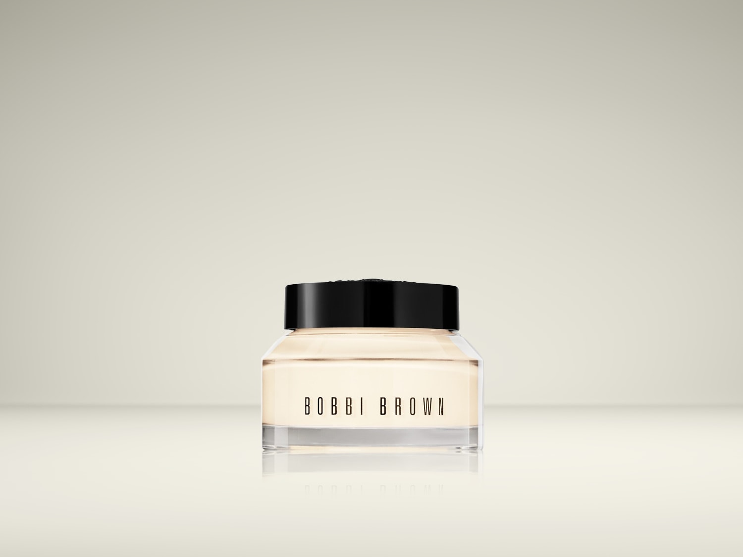 Een potje Bobbi Brown gezichtscrème met een zwarte deksel en een heldere glazen pot, gevuld met een zachte, lichtgekleurde crème.