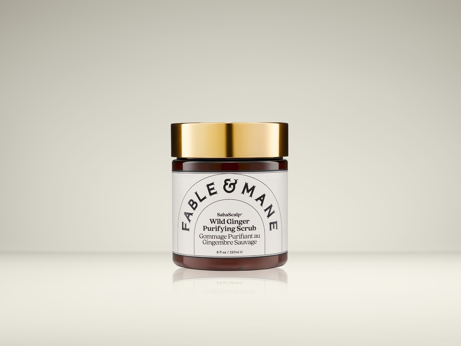 De Fable & Mane SahaScalp Wild Ginger Purifying Scrub is een bruine pot met een gouden deksel, met een wit etiket met zwarte tekst en een inhoud van 237 ml.