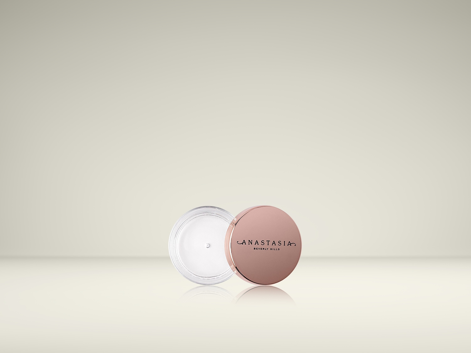 Voici un pot de crème Anastasia Beverly Hills, ouvert, avec un couvercle rose doré à côté, sur un fond beige clair.