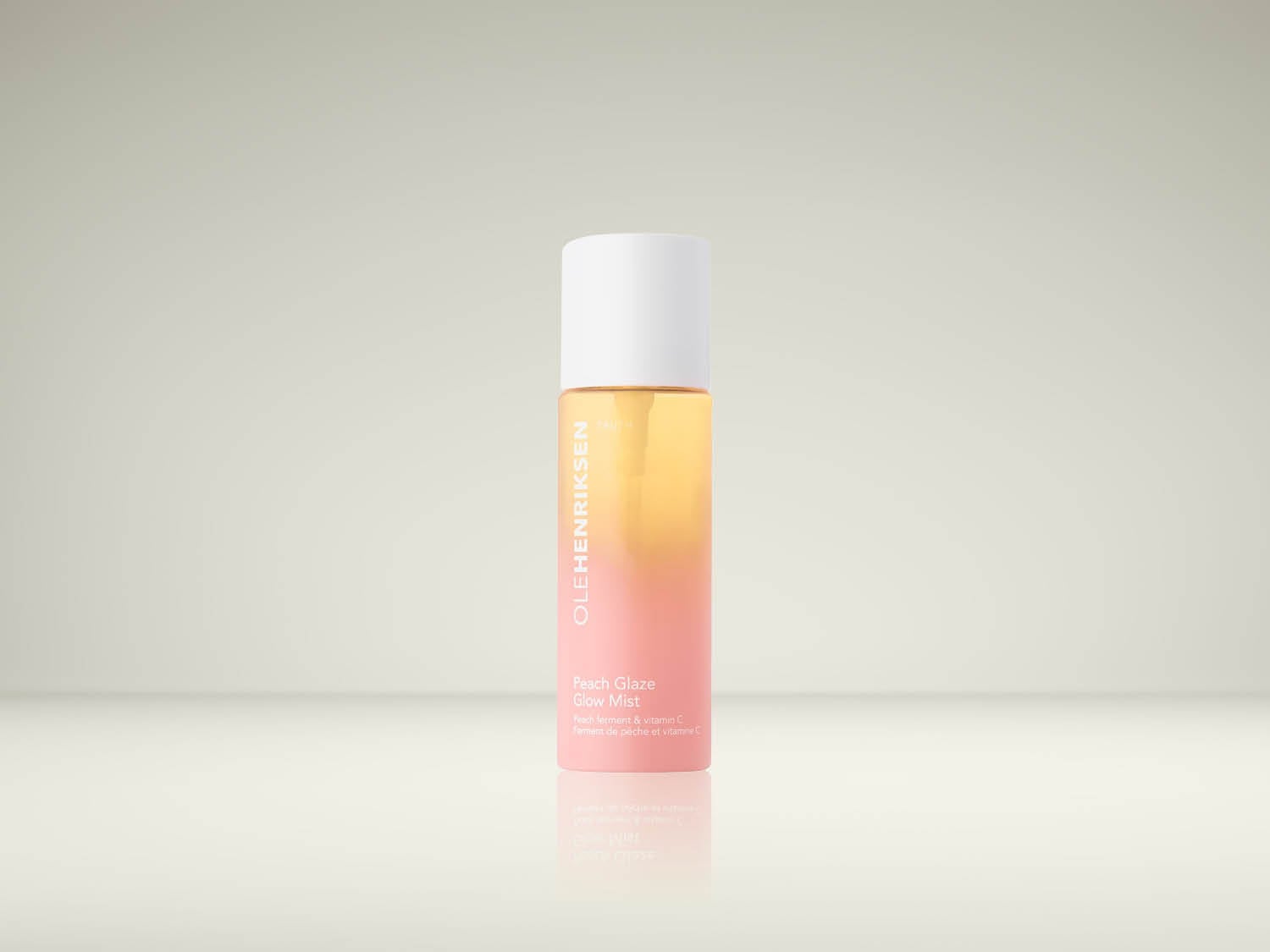 Découvrez la brume éclat OLEHENRIKSEN Peach Glaze, un flacon transparent avec un dégradé de pêche et de rose, contenant un liquide jaune-orange, enrichi en ferment de pêche et vitamine C pour un teint lumineux.