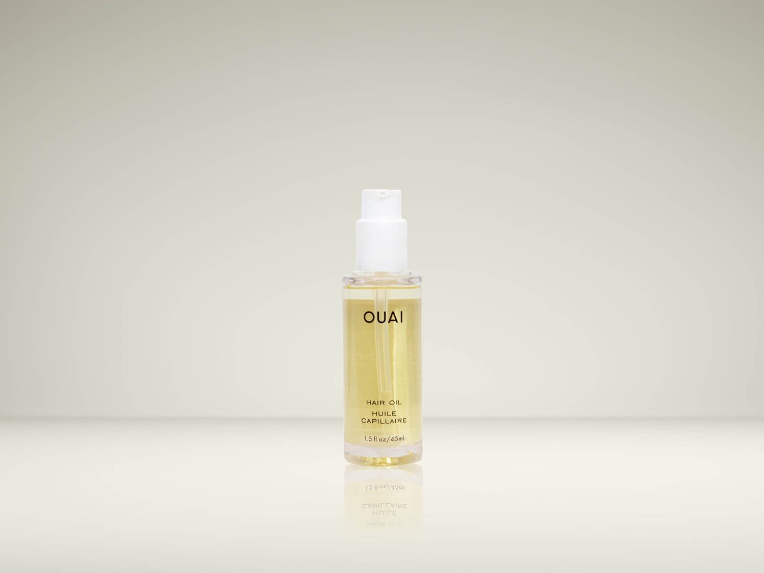 L'huile capillaire OUAI de 45 ml est présentée dans une bouteille transparente avec une pompe blanche, le liquide doré à l'intérieur reflétant la lumière.